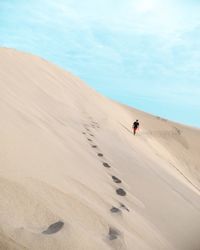 Man walking on sand dune against sky