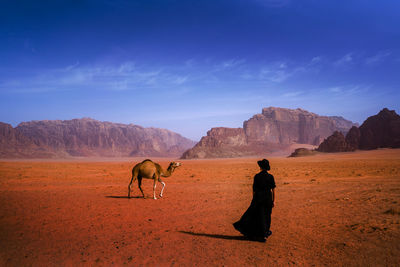 Rear view of woman standing on land with camel against mountains and sky