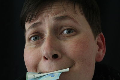 Portrait of woman with paper currency in mouth against black background