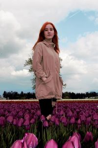 Portrait of young woman standing on field against cloudy sky