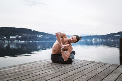 Young man relaxing on pier at lake against sky