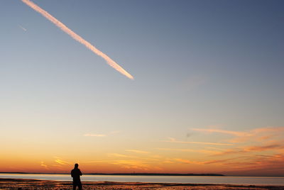 Silhouette man standing at beach against sky during sunset