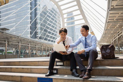 Colleagues using laptop on steps in city