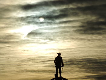 Silhouette of people standing on landscape against cloudy sky