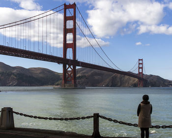 Rear view of woman standing by river against golden gate bridge