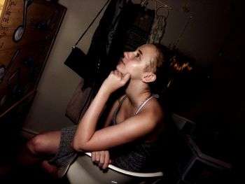 Thoughtful woman looking away while sitting on chair at home