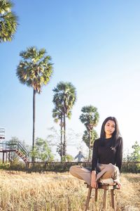 Portrait of young woman sitting on field against clear sky