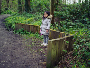 Full length of smiling young girl standing in forest park 