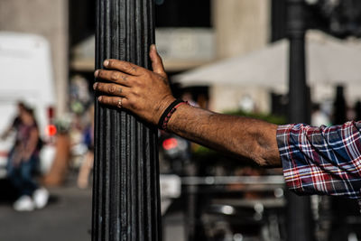 Close-up of man holding hands on pole in city