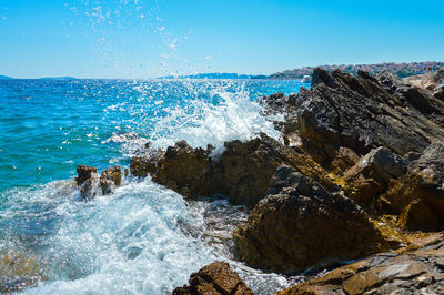 Waves splashing on rocks at shore against sky