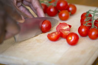 Cropped image of hands cutting cherry tomatoes on board