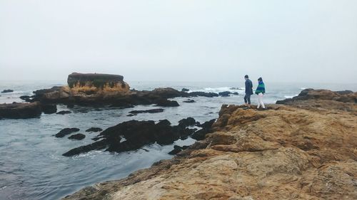 People standing on rock by sea against sky