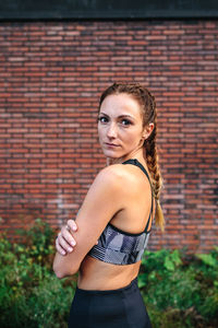 Sporty woman with boxer braids posing in front of a brick wall