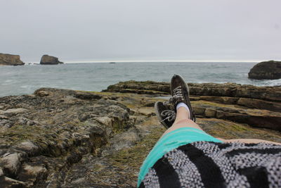 Low section of person on rock by sea against sky