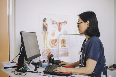 Side view of female healthcare expert using computer sitting at desk in hospital