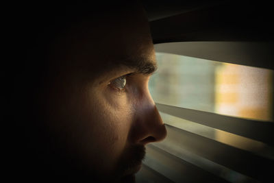 A man in a dark room looks out the window through the blinds. covert surveillance. close-up