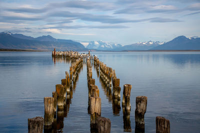 Wooden posts in lake against sky