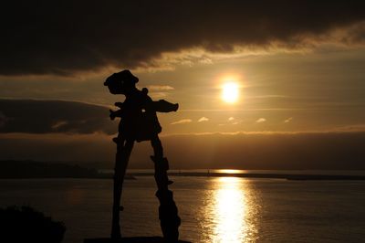 Silhouette person on sea against sky during sunset