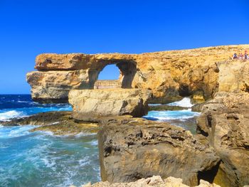 Rock formations by sea against clear blue sky