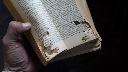 Cropped hand of man holding old torn book over black background.