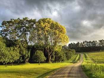 Road passing through field against cloudy sky