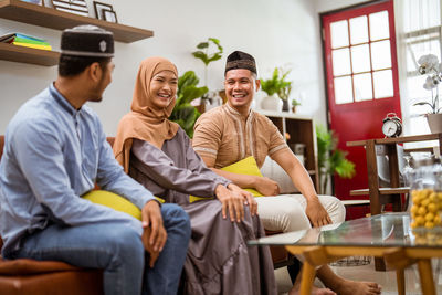 Smiling friends sitting on sofa at home