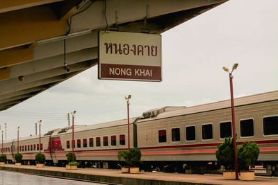Train by sign hanging from roof at railroad station platform