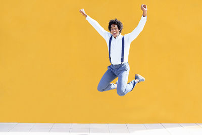 Full length of young man jumping against yellow wall