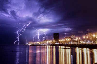 Lightning over illuminated city against sky at night