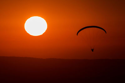 Silhouette of person paragliding against orange sky