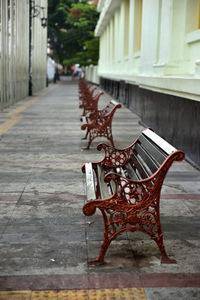 Empty bench on sidewalk by buildings in city