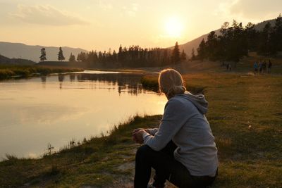 Side view of woman by lake against sky during sunset