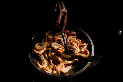 Cropped hand preparing shrimp against black background