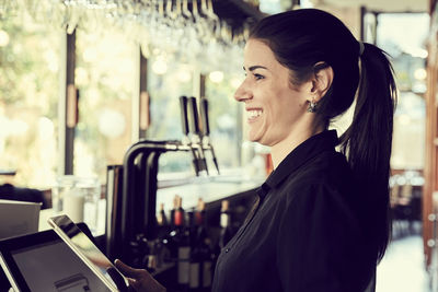 Smiling female owner with digital tablet looking away while standing in cafe