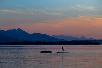 Man paddleboarding on lake against sky during sunset