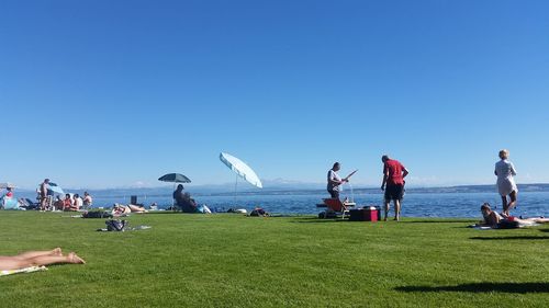 People at beach against clear blue sky