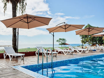 Deck chairs by swimming pool against sky