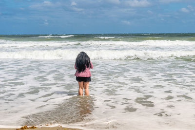 Rear view of woman standing on beach against sky