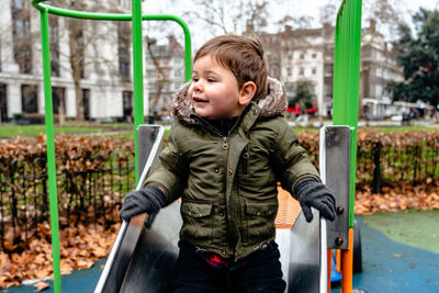 Smiling boy sitting on slide at playground during winter