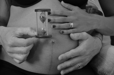 Cropped hand of husband holding hourglass while touching pregnant wife belly