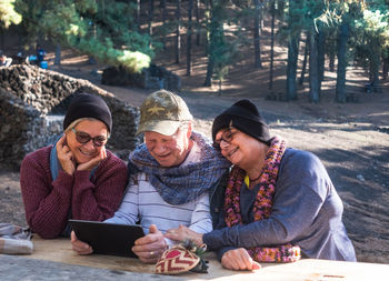 Senior man with friends using digital tablet at forest