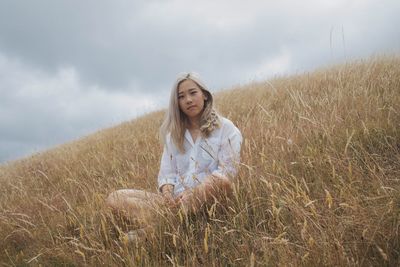 Portrait of smiling young woman sitting on field against sky