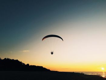 Silhouette person paragliding against sky during sunset