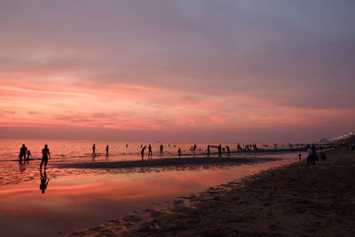 Silhouette people walking on beach against sky during sunset