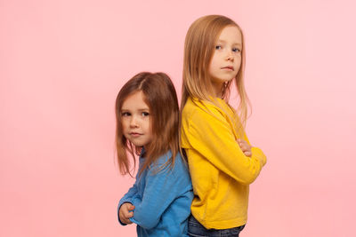 Portrait of sibling standing against peach background