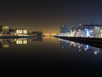 Illuminated cityscape by river against sky at night