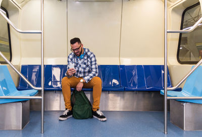 Full length of young man using mobile phone while sitting in train