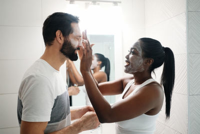 Side view of woman applying face mask to man at home