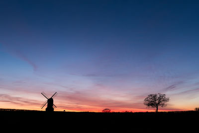 Silhouette of traditional windmill on field at sunset