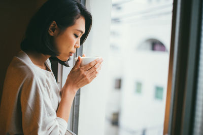 Young woman drinking water from window at home